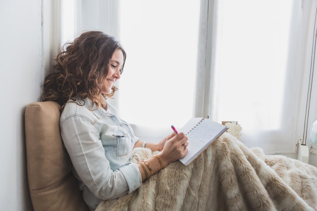 Jeune femme détendue écrivant dans son carnet pour une routine matinale anti-stress. Jeune femme détendue écrivant dans son carnet dans le cadre de sa routine matinale anti-stress.